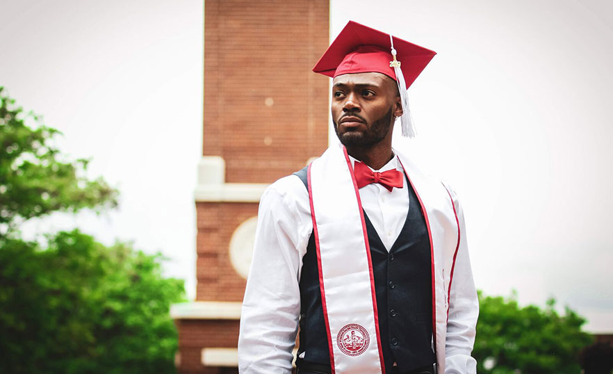 William Crandell stands in graduation cap in front of clocktower