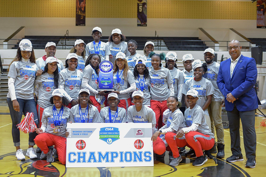 Track team stands with trophy and banner